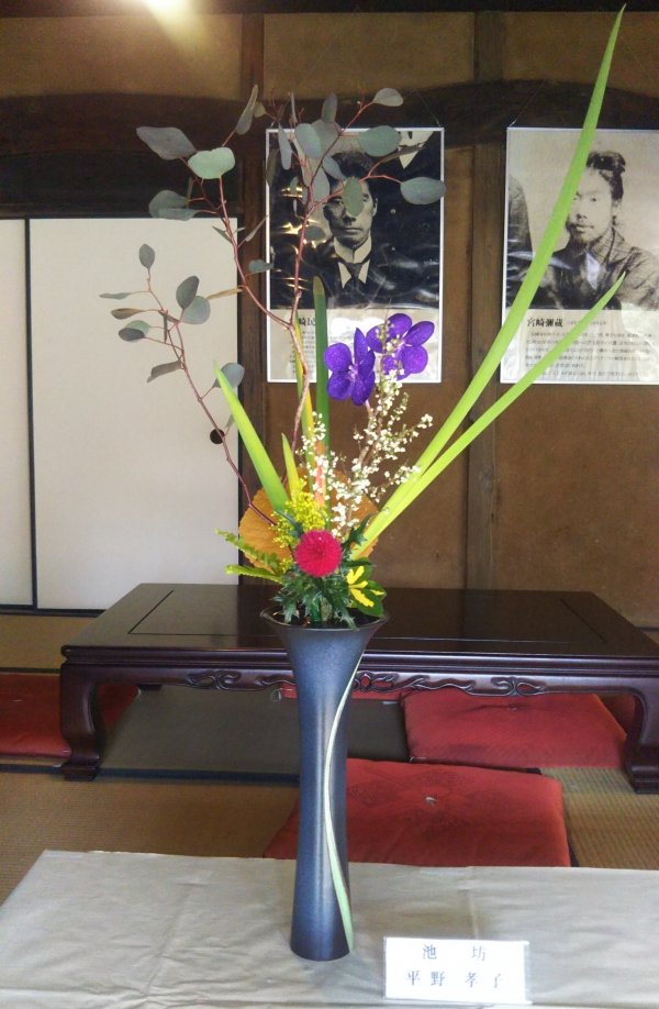 画像ファイル：「作品2:赤紫色のアザミの花をメインに紫色のランの花を添え、細長い葉と深緑色の葉の枝で高さのある作品の写真」の詳細を見る